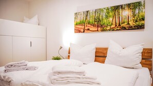 Ein ordentlich bezogenes Bett mit weißen Leinen und Kissen, ein Holz-Kopfteil und ein Waldgemälde an der Wand.