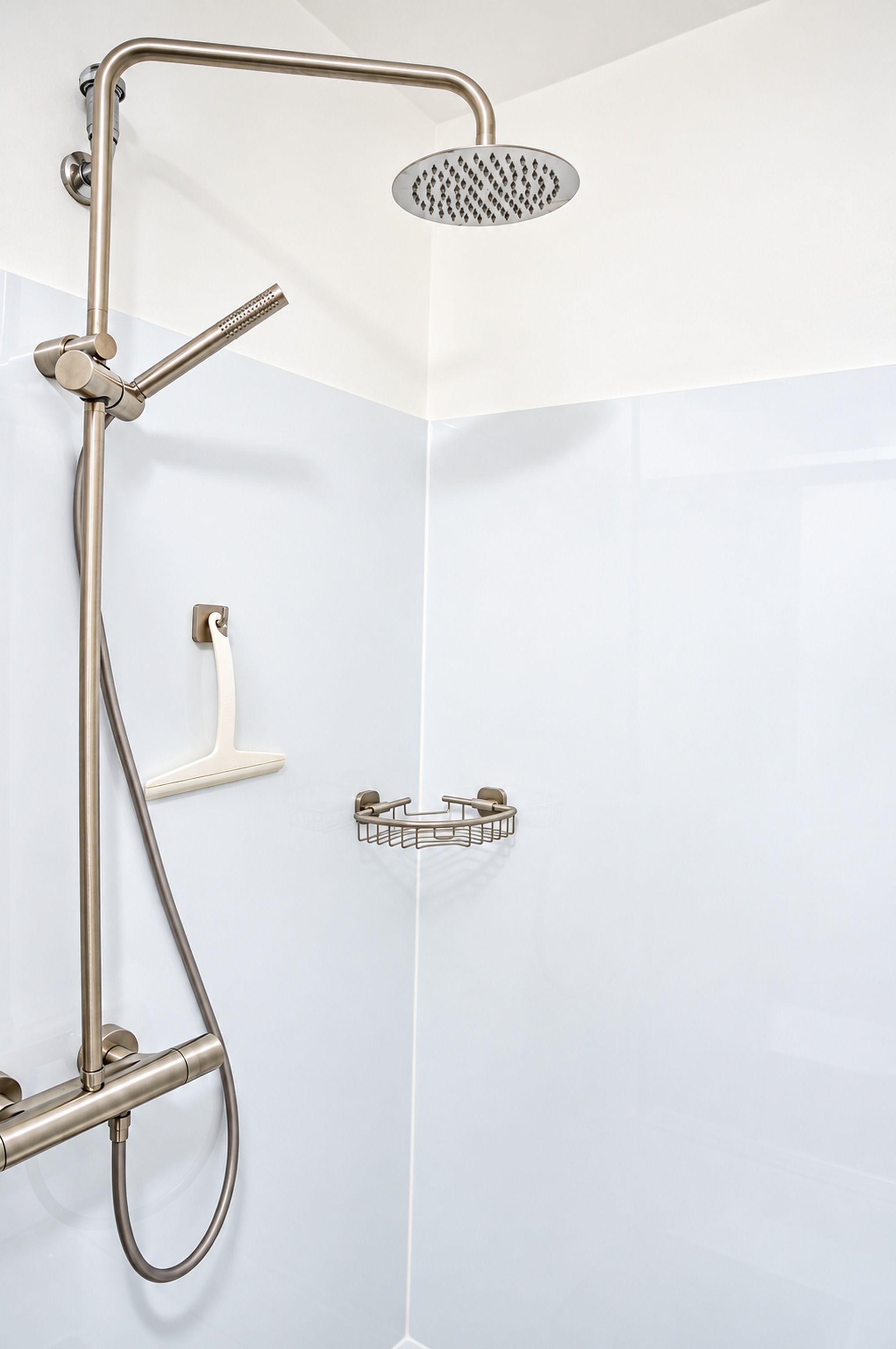 A corner shower with a handheld showerhead, a wall-mounted faucet, and a small shelf.