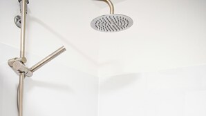 Eine moderne Dusche mit Handbrause, Deckenbrause und einem Wandregal.