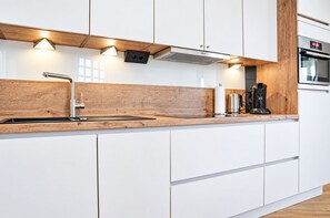 A modern kitchen with white cabinetry, a wooden countertop, a built-in stove, and a coffee maker. - Schöne Ferienwohnung mit Balkon Direkt am Erlebinsberg Kappe (Winterberg)