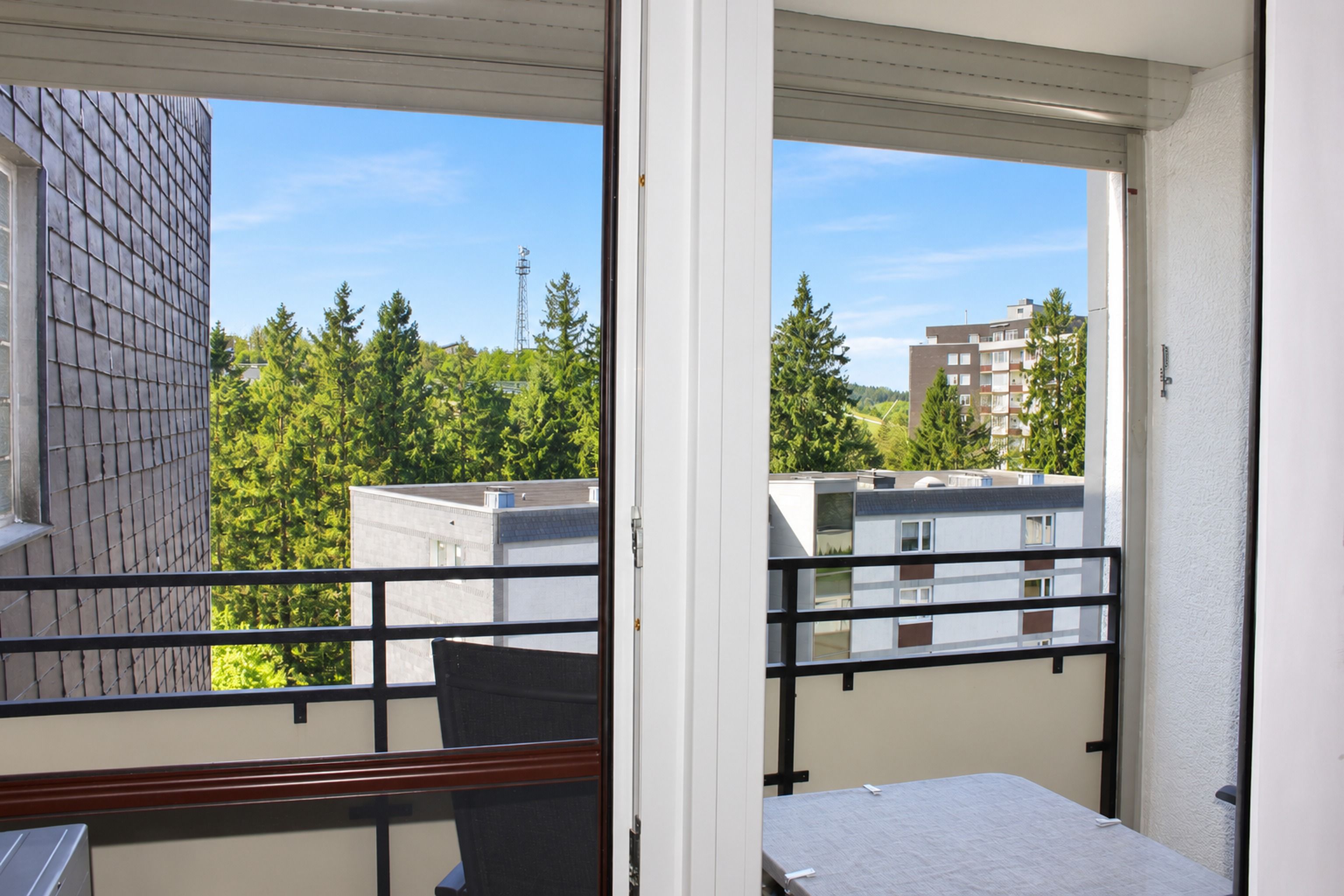 A balcony with a view of a building with a brick facade and a tree-lined street.