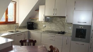 A kitchen with white cabinets, a granite countertop, a black coffee maker, and a stainless steel oven. - Maison Située Dans le Vignoble, Appartement à L'étage Avec Entrée Indépendante (Soultzmatt)