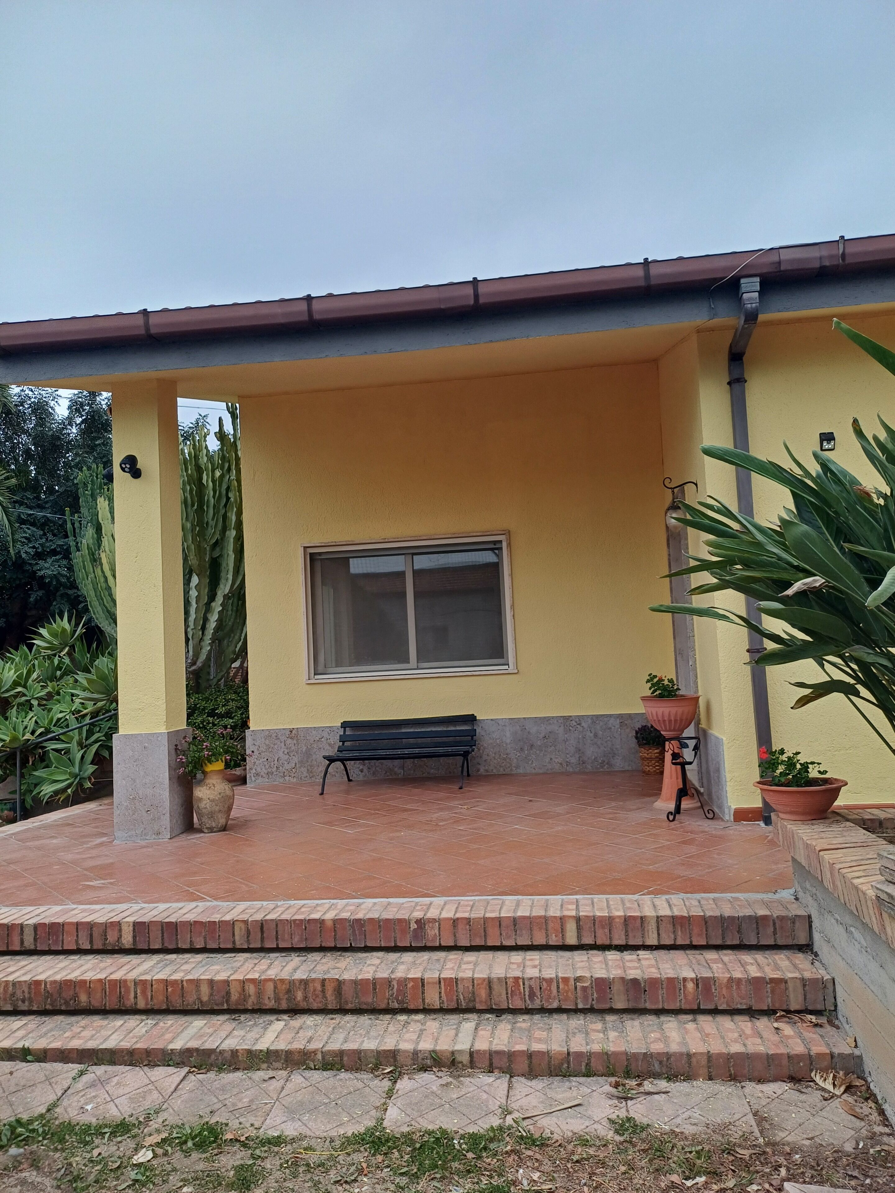 A building with a yellow exterior, a window, a bench, and potted plants.