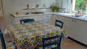 A kitchen with white cabinets, a tiled backsplash, a dining table with chairs, and a window with plants.