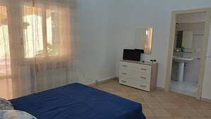 A bedroom with a bed, a dresser, a TV, and a bathroom visible through an open door.