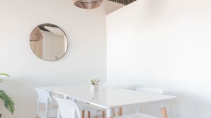 A modern dining area with a white table and chairs, a round mirror on the wall, and a small plant on the table. - MOT Rentals + Madero Azopardo 'C' Lux 1 Bd (Puerto Madero)