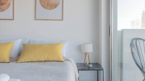 A bedroom with a bed, pillows, a nightstand, a lamp, and a view of the city through a window. - MOT Rentals + Madero Azopardo 'C' Lux 1 Bd (Puerto Madero)