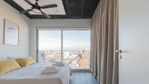 A hotel room with a bed, a ceiling fan, a large window with curtains, and a view of the cityscape. - MOT Rentals + Madero Azopardo 'C' Lux 1 Bd (Puerto Madero)
