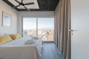 Une chambre d’hôtel avec un lit, un ventilateur de plafond, une grande fenêtre avec des rideaux et une vue sur le paysage urbain.