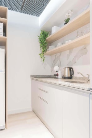 A modern kitchen with white cabinets, a marble backsplash, and a coffee maker on the counter.