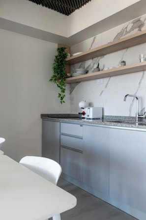 A modern kitchen with marble backsplash, wooden shelves, and a white countertop. - MOT Rentals + Madero Azopardo 'D' Lux 1 Bd (Puerto Madero)