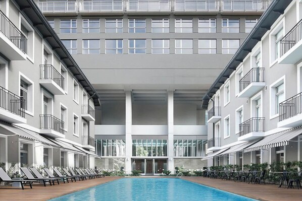 A modern hotel with a central swimming pool, multiple balconies, and a clean, contemporary design.