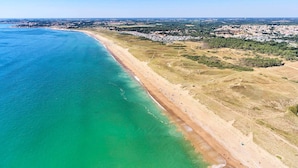 An aerial view of a coastal area with a sandy beach, clear turquoise waters, and a mix of residential and natural landscapes.