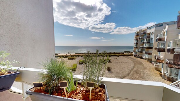 A balcony with a view of the sea, a sandy beach, and a modern building with balconies.