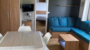 Un espacio habitable compacto con una mesa de comedor, un sofá, un televisor y una cama litera.