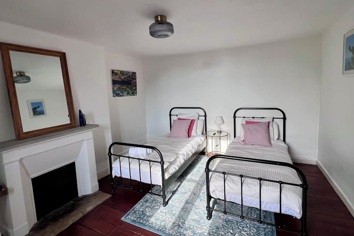 Un dormitorio con dos camas individuales, una chimenea, un espejo y una pequeña mesa con lámpara.