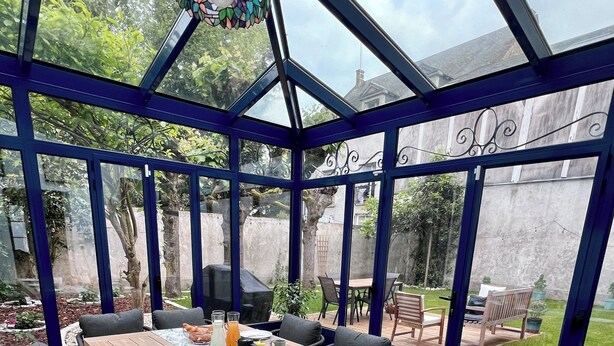A covered patio with a wooden table set for dining, surrounded by chairs, and a view of the backyard. - Maison POL Amboise (Amboise)