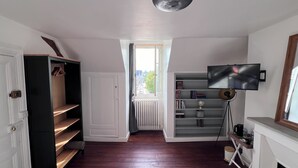 A room with a wooden floor, a white door, a black wardrobe, a bookshelf, a TV mounted on the wall, and a fireplace. - Maison POL Amboise (Amboise)