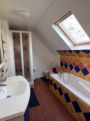 A bathroom with a skylight, a white sink, a bathtub, and a toilet.