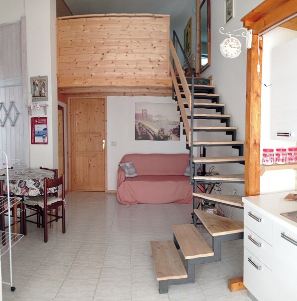 A compact living space with a dining area, a sofa, a staircase, and a kitchen area.