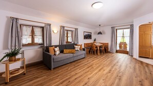 Amplia sala de estar con sofá gris, mesa de comedor de madera y un ventanal con cortinas.