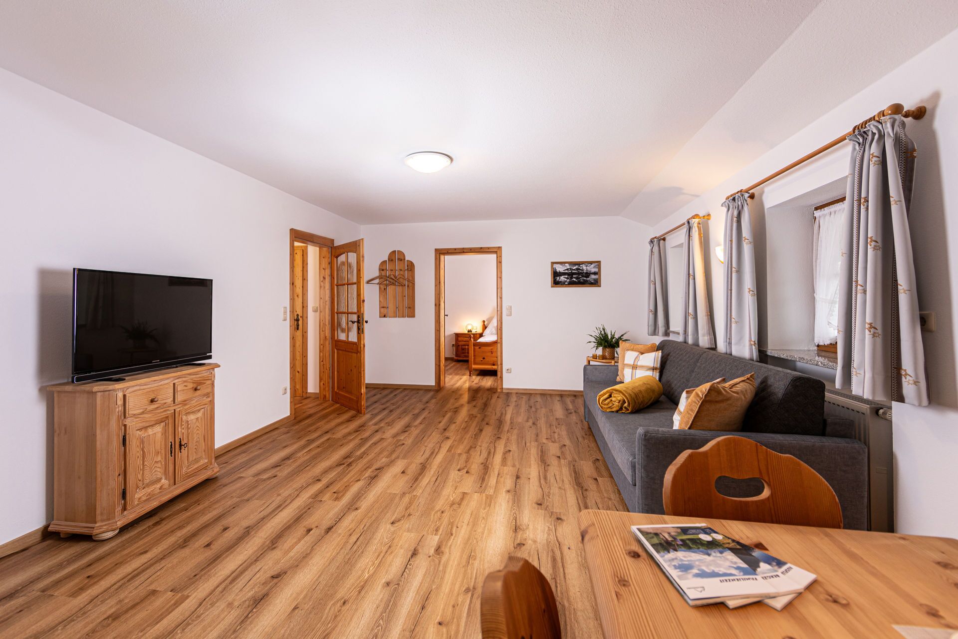 A modern living room with a flat-screen TV, wooden cabinet, and a sofa with cushions.