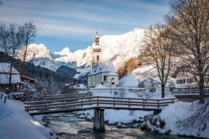 Un puente cubierto de nieve sobre un río, con una iglesia y montañas al fondo.