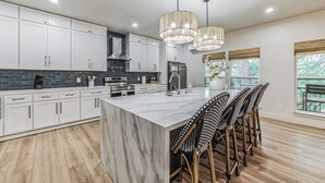Une cuisine moderne avec des meubles blancs, un îlot en marbre et un coin repas doté de chaises en osier.