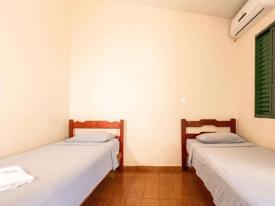 Una habitación pequeña y limpia con dos camas individuales, suelo de baldosas y aire acondicionado instalado en la pared.