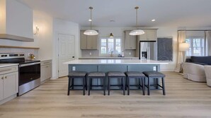 Cocina moderna con una isla central, taburetes de bar e iluminación colgante.