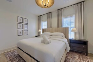 A neatly arranged bedroom with a large bed, bedside lamps, a nightstand, and framed pictures on the wall.