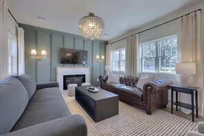 Una sala de estar con sofá, mesa de centro, chimenea, televisor y candelabro.