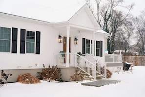 Una casa blanca con un porche cubierto, una escalera y un patio cubierto de nieve.