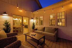 An outdoor patio with a sofa, chairs, and a table, featuring string lights and a glass door leading to an interior space.