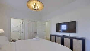 Habitación de hotel con una cama, un televisor instalado en la pared y una puerta que da a un baño.