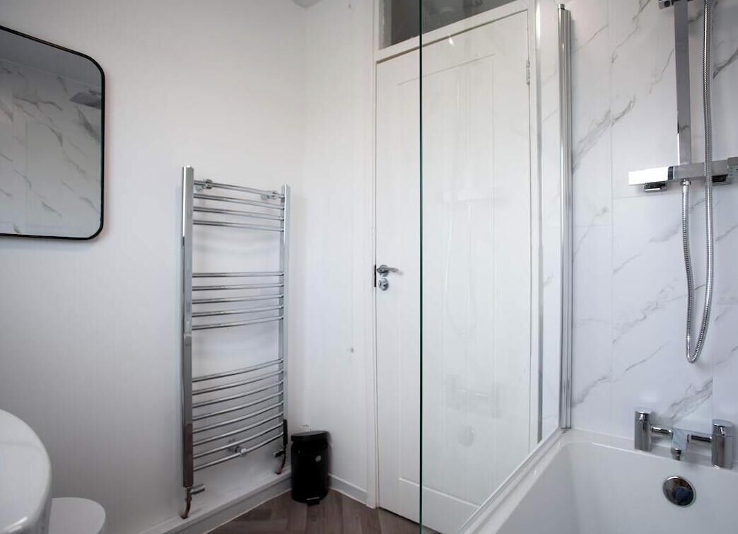 A bathroom with a glass-enclosed shower, a white toilet, a towel rack, and a marble wall.