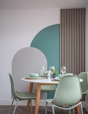 Un espace repas comprenant une table ronde, quatre chaises et un mur avec des lambris en bois verticaux.