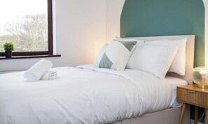 A neatly made bed with white linens, a teal-colored headboard, and a bedside table with a lamp. - The Lampton - Modern - Gibside - Smart Tv - WIFI (County Durham)