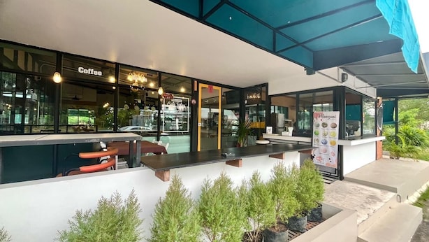 Un espace extérieur aménagé avec des tables et des chaises, un café avec une enseigne et un panneau affichant le menu.