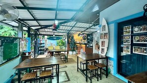 Un café avec des tables et des chaises en bois, une exposition de planches de surf et un menu écrit à la craie.