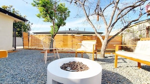 Un espace extérieur aménagé avec un foyer, deux chaises en bois et un banc.