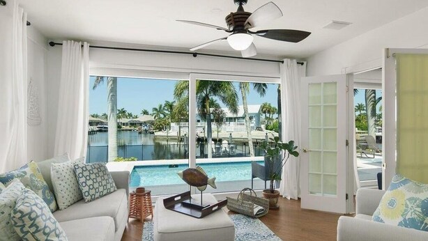 A living room with a view of a pool, a ceiling fan, and a large window. - Waterfront 3BR/2BA Marco Island home with heated pool, WiFi, and kitchen. (Marco Island)