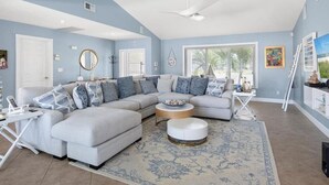 A living room with a sectional sofa, a round coffee table, and a large window providing natural light. - Waterfront 3BR/2BA Marco Island home with heated pool, WiFi, and kitchen. (Marco Island)