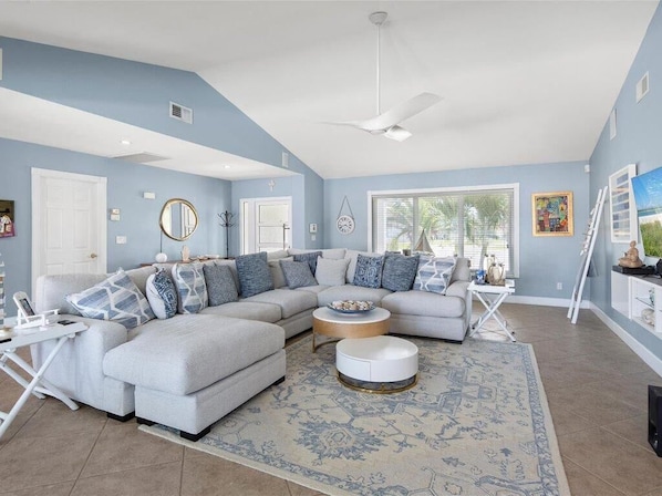 A living room with a sectional sofa, a round coffee table, and a large window providing natural light. - Waterfront 3BR/2BA Marco Island home with heated pool, WiFi, and kitchen. (Marco Island)