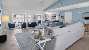 A spacious living room with a large grey sofa, a coffee table with decorative jars, and a view of the outdoor area. - Waterfront 3BR/2BA Marco Island home with heated pool, WiFi, and kitchen. (Marco Island)