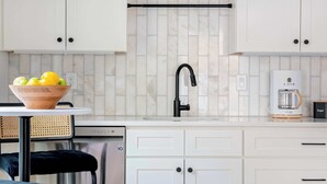Une cuisine moderne avec des meubles blancs, un robinet noir et une machine à café.