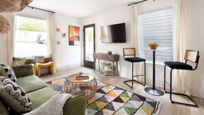 Un salon moderne comprenant un canapé, une table basse, un téléviseur et deux tabourets de bar.