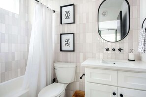 A modern bathroom with a white tiled wall, a white toilet, a white sink with a mirror above it, and framed artwork on the wall. - Champagne Wishes (Atlanta)