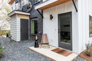 Een modern huis met een grijze gevel, een houten terras en een zwarte deur.
