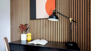 Un bureau avec un livre, une lampe et des objets décoratifs, le tout placé devant un mur en bois composé de lattes verticales.